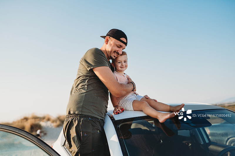 年轻的父亲和他的儿子坐在车顶上图片素材