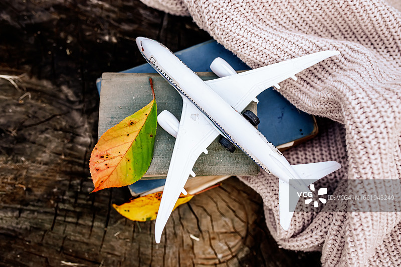 在秋天旅行。旧的古书上的飞机，木制背景上的针织毛衣和黄色的秋叶。俯视图图片素材