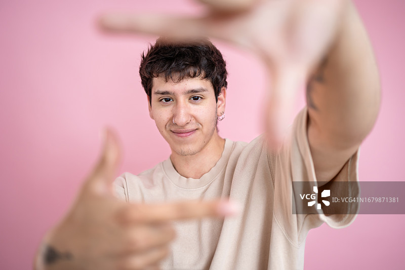 年轻男子休闲装制作的相框与手在粉红色的背景。图片素材