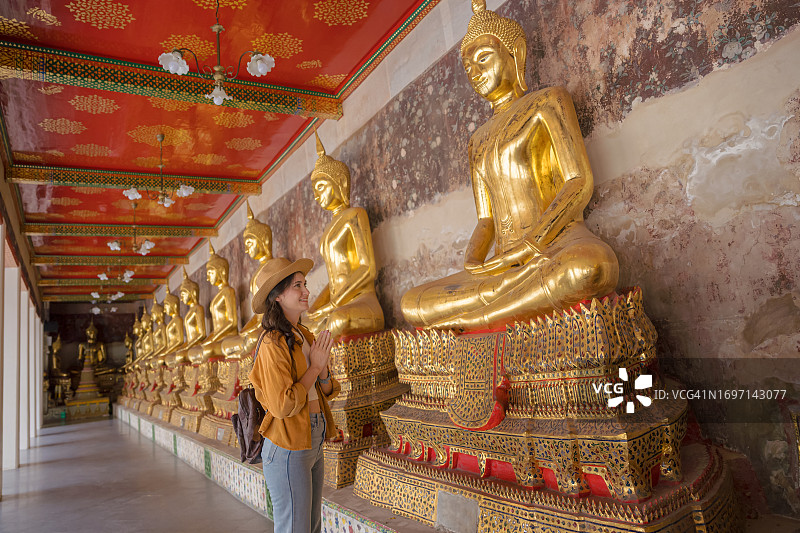 在曼谷卧佛寺，一名女游客在一排佛像旁真诚地祈祷。图片素材
