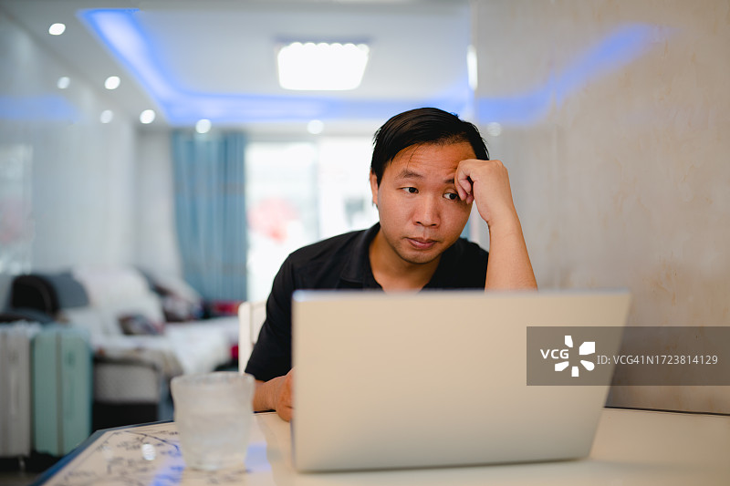 一个亚洲男人看着电脑，一副严肃的表情，在家里担心和焦虑图片素材