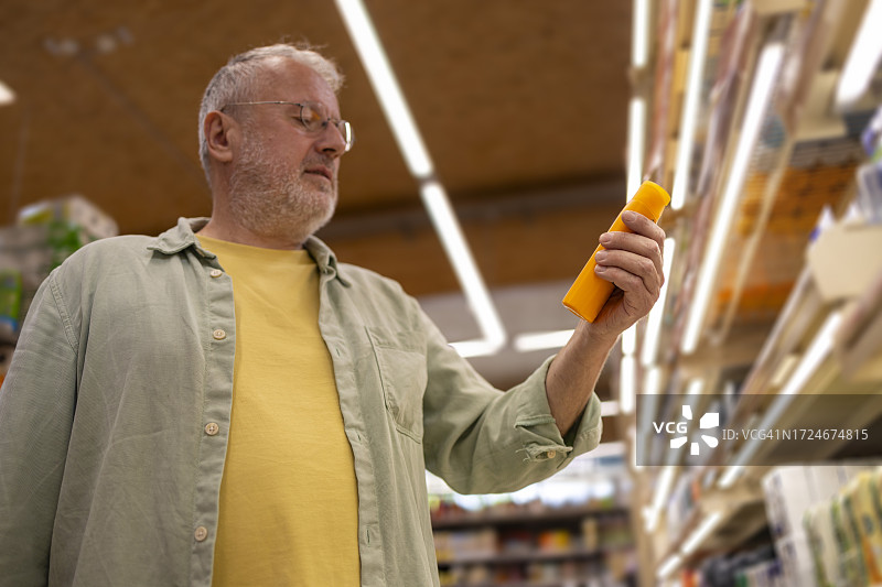 一个成熟的男人拿着洗发水在超市的货架上看标签图片素材