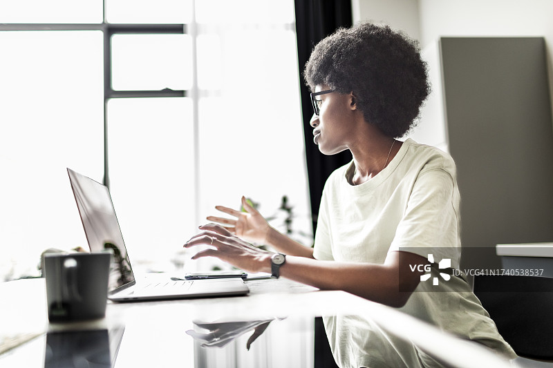 年轻的黑人女性在家厨房用笔记本电脑工作图片素材