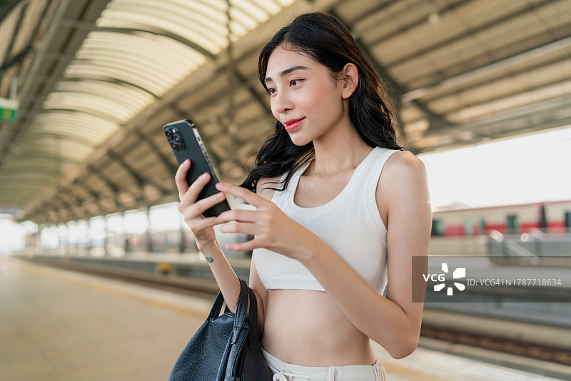 年轻的亚洲女子在地铁站台等候公共交通列车时使用手机图片素材