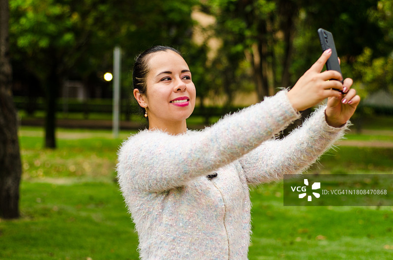 一名女子在公园里用智能手机自拍图片素材