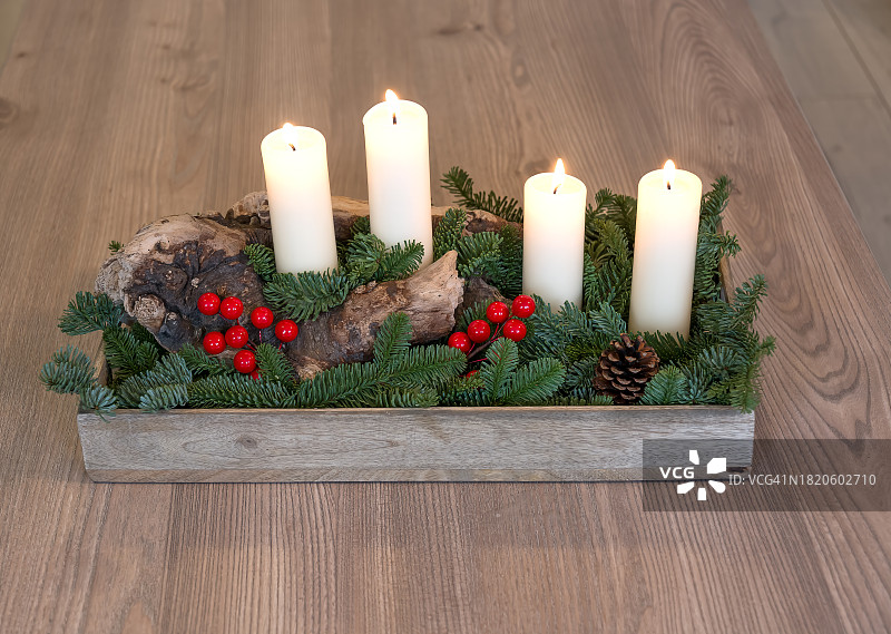 这是一个手工制作的降临节或圣诞节构图的例子，有四支燃烧的蜡烛，在一个老树干上，周围是绿色的云杉树枝和红色的浆果。降临节、圣诞节和新年的概念。图片素材