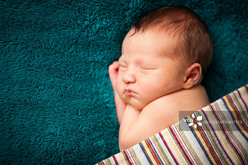 新生男婴在条纹毯子下安静地睡觉图片素材
