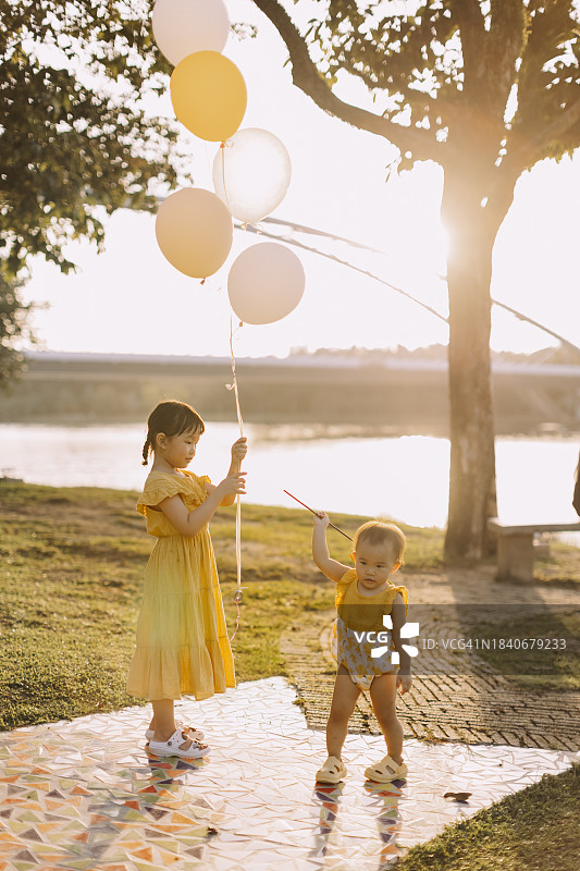 两个亚洲小女孩在花园公园里玩气球和风车玩具。库存图片图片素材
