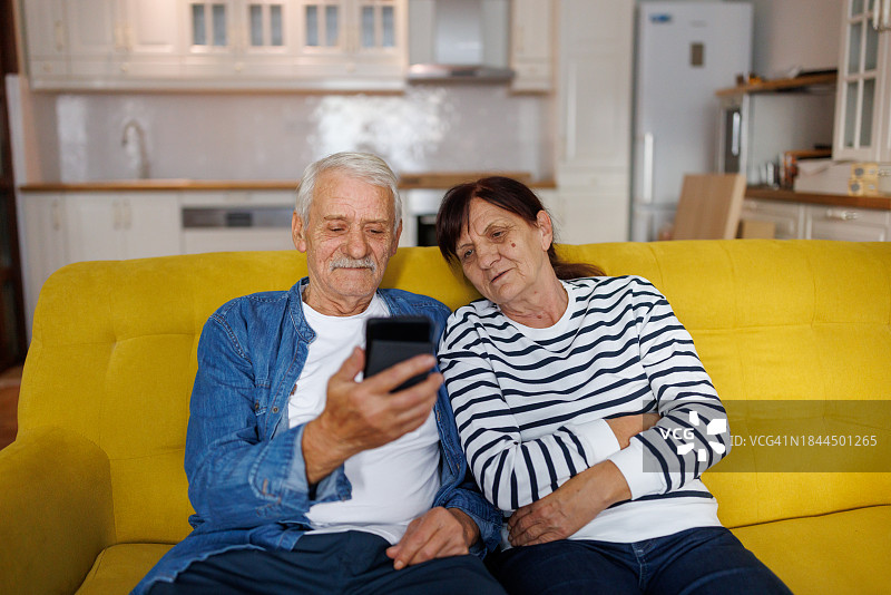 幸福的老年夫妇在新公寓的沙发上放松地自拍图片素材