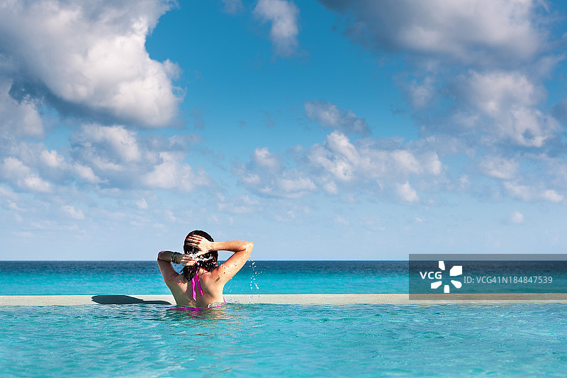 年轻女子在加勒比海滩度假酒店享受无限游泳池图片素材