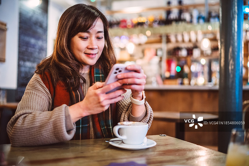 美丽的亚洲女人在咖啡馆喝咖啡休息时使用智能手机图片素材