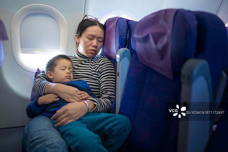 旅途中的温馨时刻:中国妈妈和多种族小孩在飞机上小睡图片素材