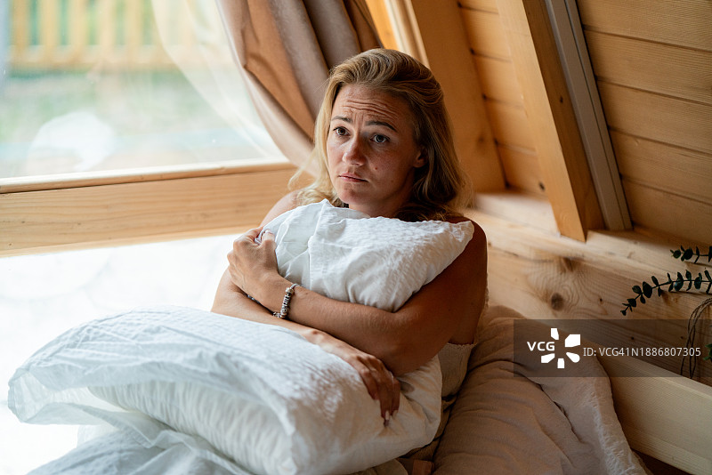 焦虑的女人坐在床上抱着枕头图片素材