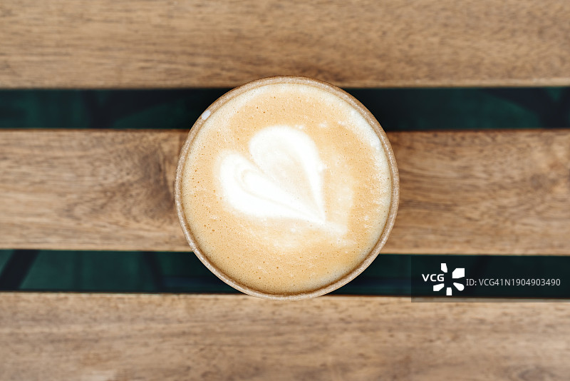 一杯卡布奇诺或拿铁咖啡，木质背景上有心形图案图片素材