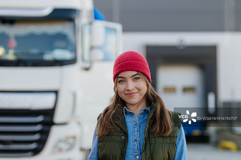 卡车前的女性职业卡车司机的肖像，看着镜头，微笑着。女司机的概念，长途卡车运输。图片素材