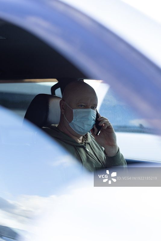 一个成熟的男人坐在车里，脸上戴着医用口罩图片素材