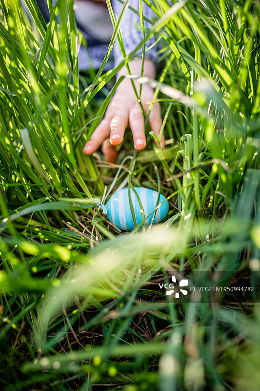 一个小孩伸手去拿复活节彩蛋。图片素材