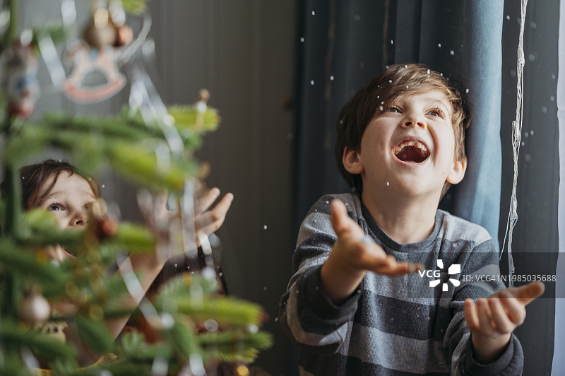 顽皮的男孩在家里的圣诞树旁抓假雪图片素材