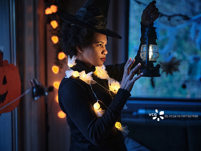 穿着女巫服装的黑人妇女在家里看着灯笼。图片素材
