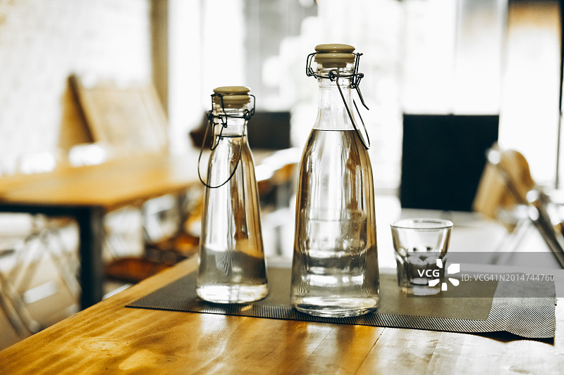 在舒适的咖啡馆设置木桌上的极简主义水瓶。图片素材