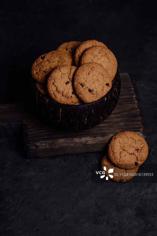 燕麦饼干和巧克力片在一个碗里，在黑暗的背景上有半个椰子图片素材