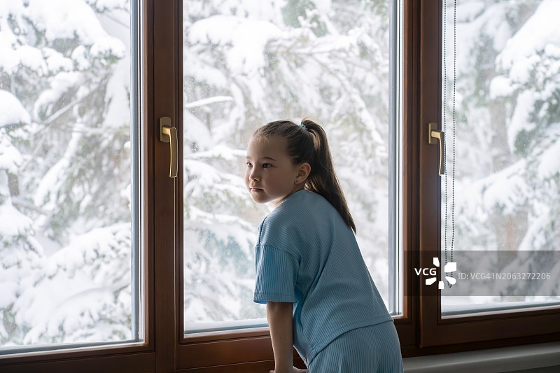 一个穿着蓝色西装的女孩站在一扇大窗户的背景下，窗外是冬天的风景。图片素材