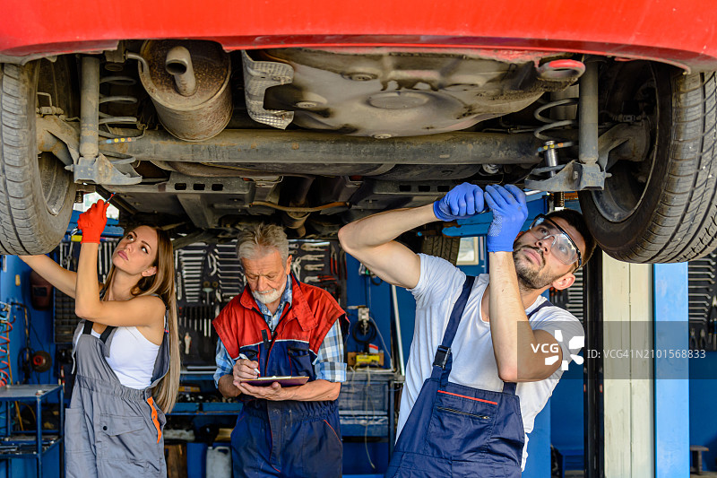 一对汽车修理工和一位资深男同事在机械车间的吊车下工作。图片素材