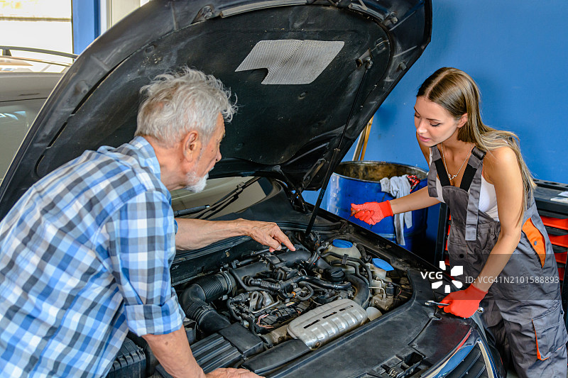 一位经验丰富的汽车修理工站在汽车维修站，在正在学习的年轻女同事的帮助下解决问题。图片素材