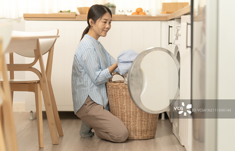 亚洲女性周末在家用洗衣机洗衣服图片素材