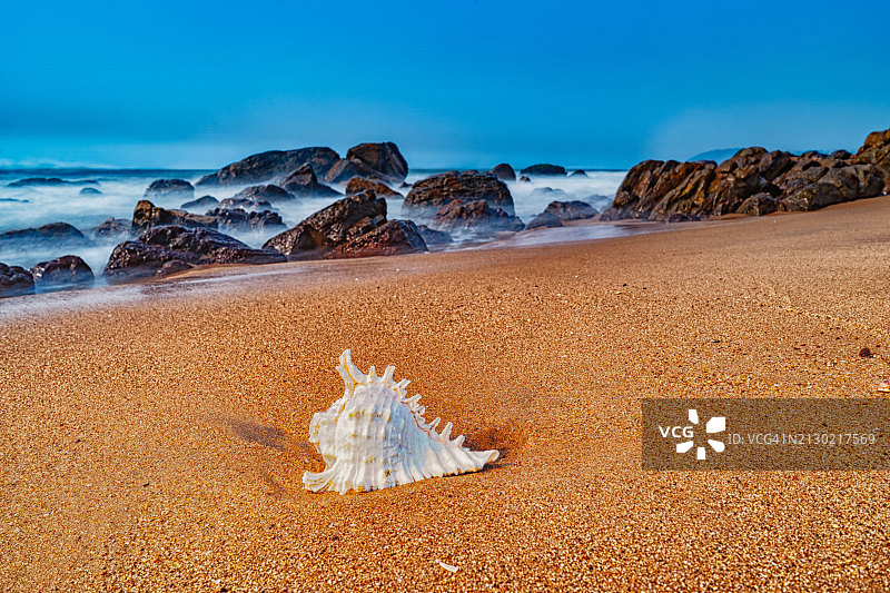 一个抽象的长曝光拍摄的岩石海滩，乳白色的水流过岩石和海螺冲上岸。图片素材