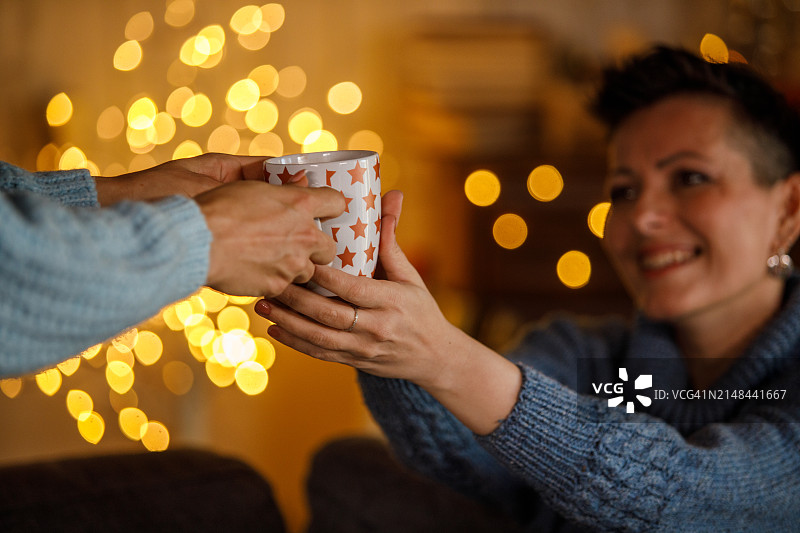 一个女人给她的朋友一杯咖啡，在舒适的家里一起享受圣诞节图片素材
