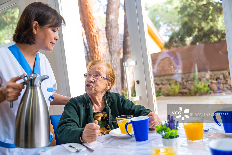在老年病院里吃早餐时，护士和一位老年妇女交谈图片素材
