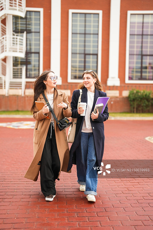 两个女学生拿着笔记本去大学校园上课图片素材