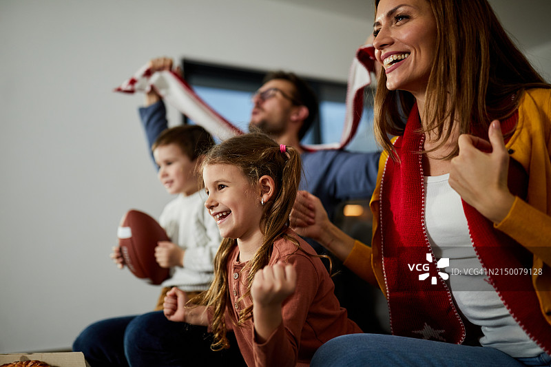 欢乐的一家人在家里看电视上的橄榄球比赛。图片素材