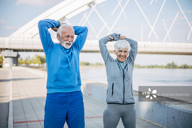 一对穿着运动服的老年夫妇在公园里伸展身体。图片素材