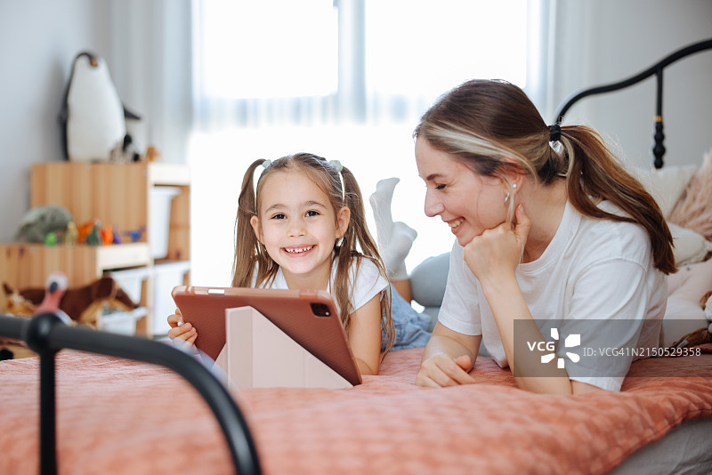 母亲和女儿一起躺在床上看他们的数码平板电脑图片素材