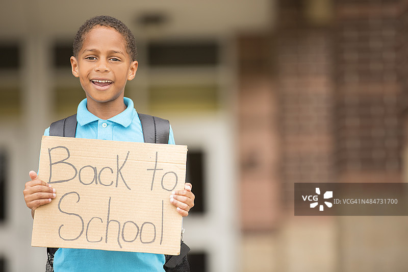 非洲后裔，一个小男孩拿着学校的牌子。图片素材