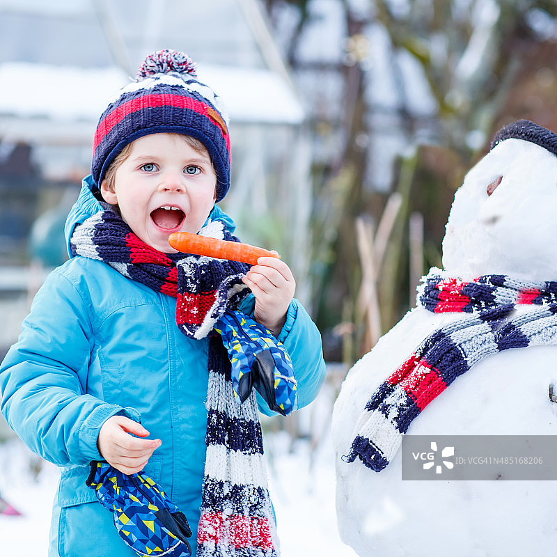 滑稽的小男孩穿着五颜六色的衣服在户外堆雪人图片素材
