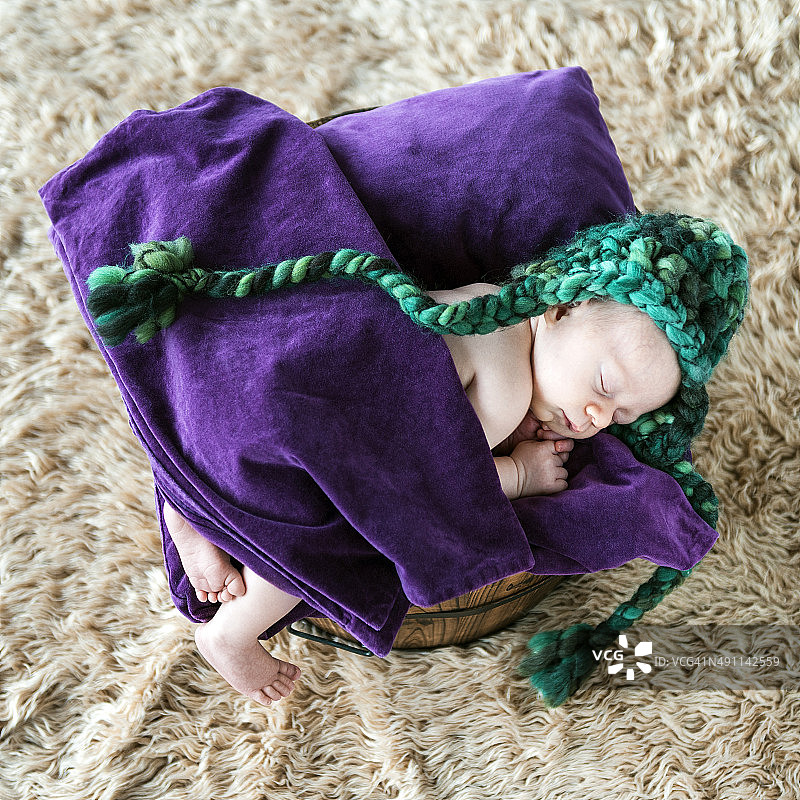 刚出生的小男孩躺在紫色的枕头上，盖着毯子睡得很安稳图片素材
