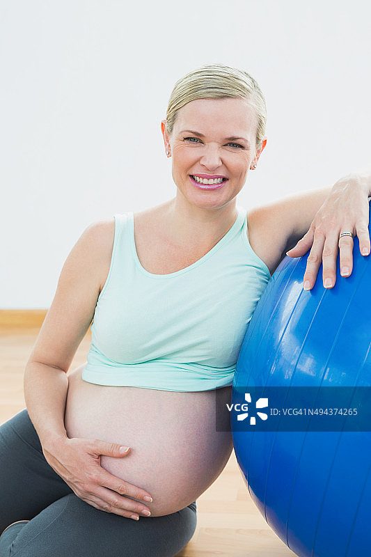 快乐的孕妇靠在锻炼球抱着她的肚子图片素材