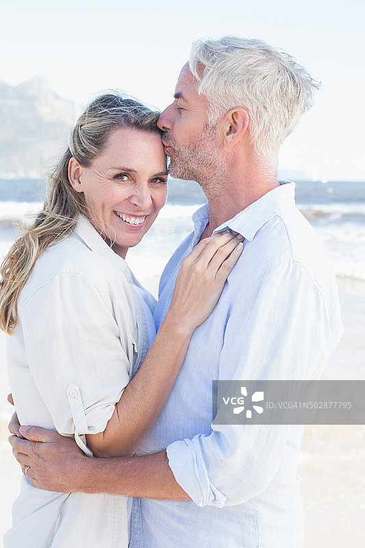 一名男子在海滩上亲吻他微笑的伴侣的前额图片素材