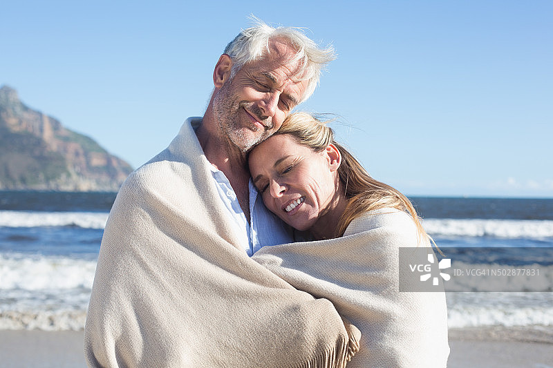 在海滩上，一对微笑的夫妇裹着毯子图片素材