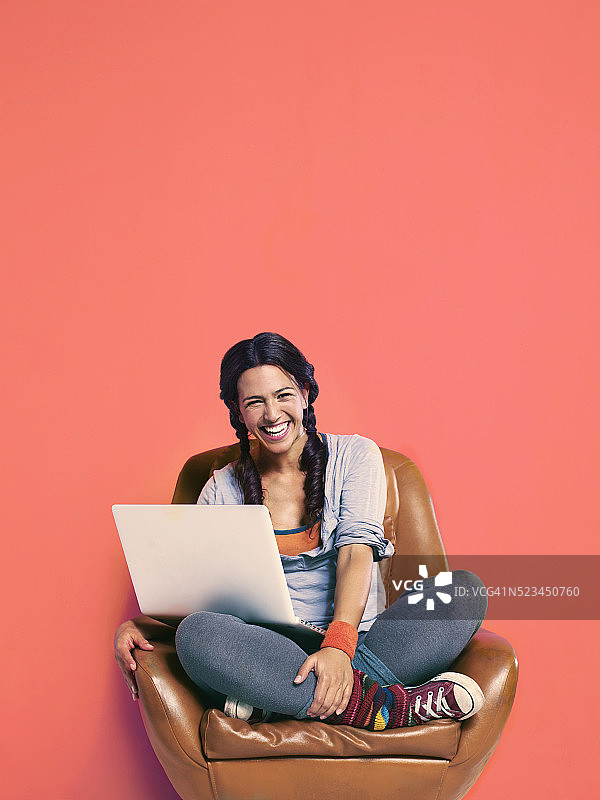 少女(16-17岁)坐在扶手椅上用笔记本电脑的工作室肖像图片素材