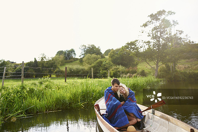 年轻夫妇裹在毯子里，在河里划船图片素材