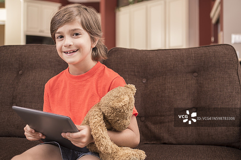 孩子在家阅读数字平板电脑与泰迪熊。图片素材