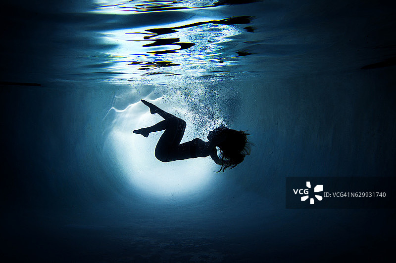 一名水下女模特的剪影肖像在加州圣地亚哥的一个游泳池里跳舞。图片素材