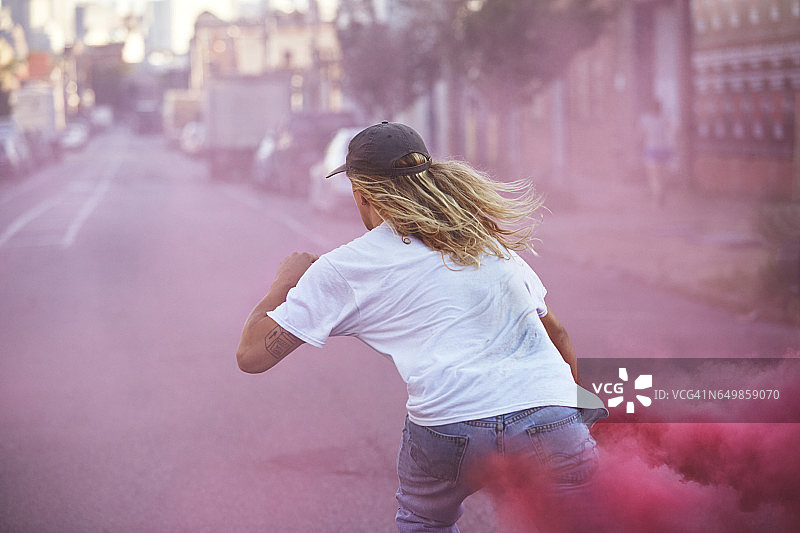 年轻的男子滑板穿着白色t恤携带一个粉红色的照明弹，他滑下街道图片素材