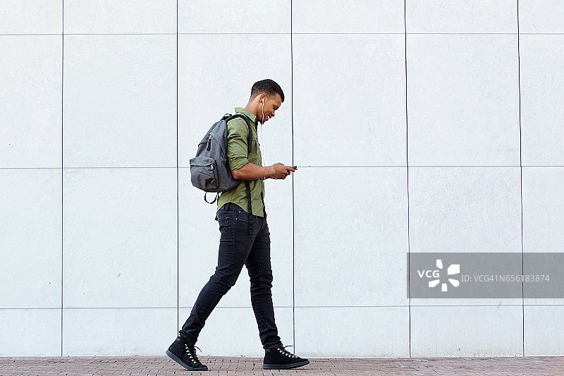 微笑的男人背着背包走路智能手机和耳机图片素材