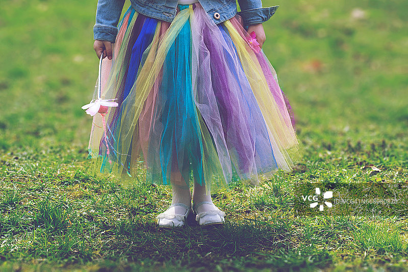 小女孩穿着五颜六色的短裙站在绿色的草地上，手里拿着魔杖图片素材