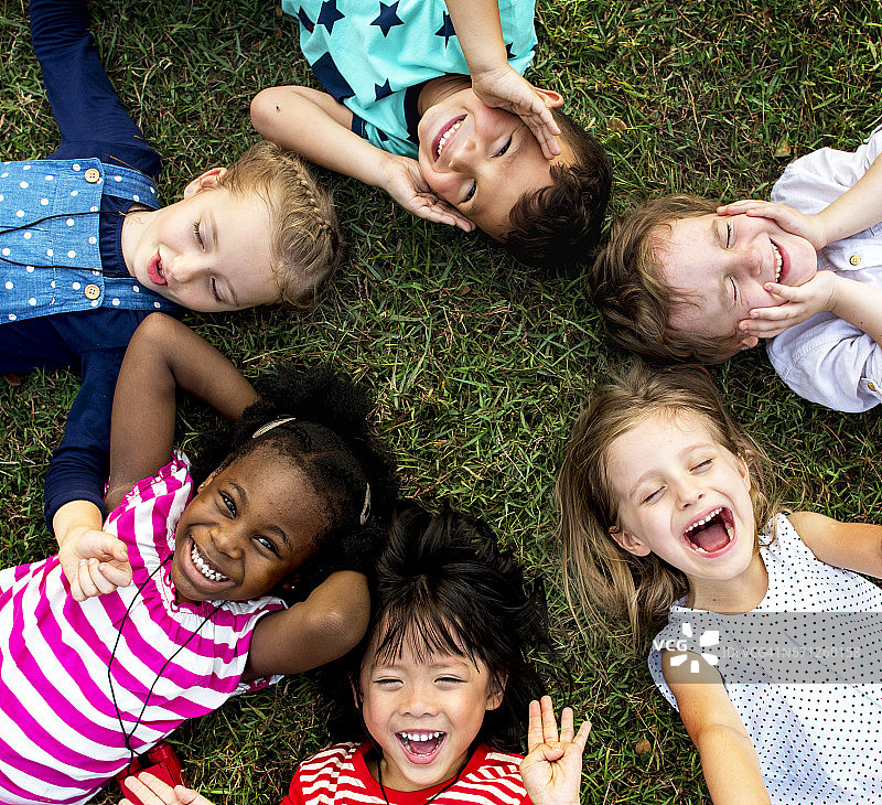 一群幼儿园的孩子躺在公园的草地上，微笑着放松图片素材